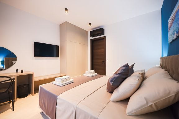 Moderne Hotelzimmer mit Doppelbett, Schreibtisch und Fernseher an der Wand.