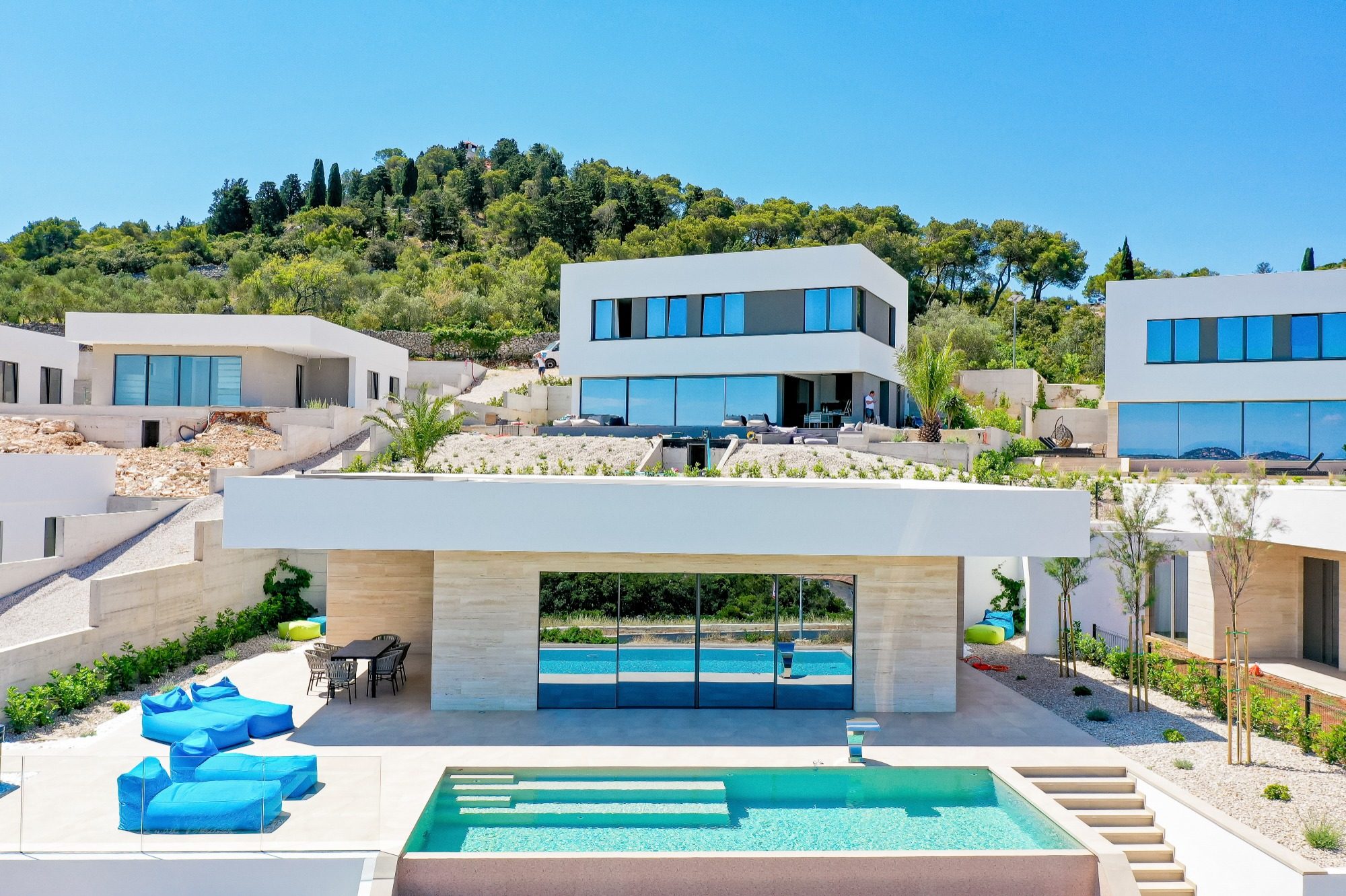 Moderne Villa mit Pool und Lounge-Bereich, umgeben von grünen Hügeln.