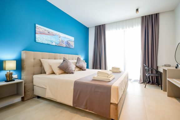 Helles Schlafzimmer mit blauem Wandton, Doppelbett und modernen Möbeln.