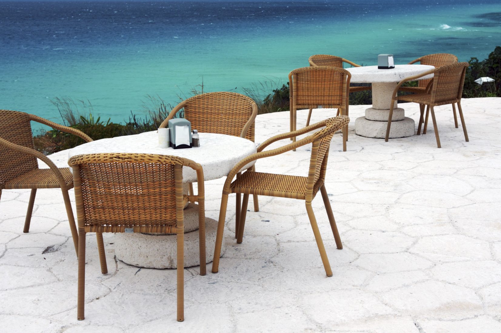 Tische und Stühle aus Rattan mit Blick auf das blaue Wasser des Meeres.