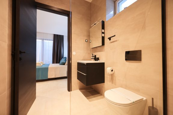 Modernes Badezimmer mit Toilette, Waschbecken und Zugang zu einem Schlafzimmer.